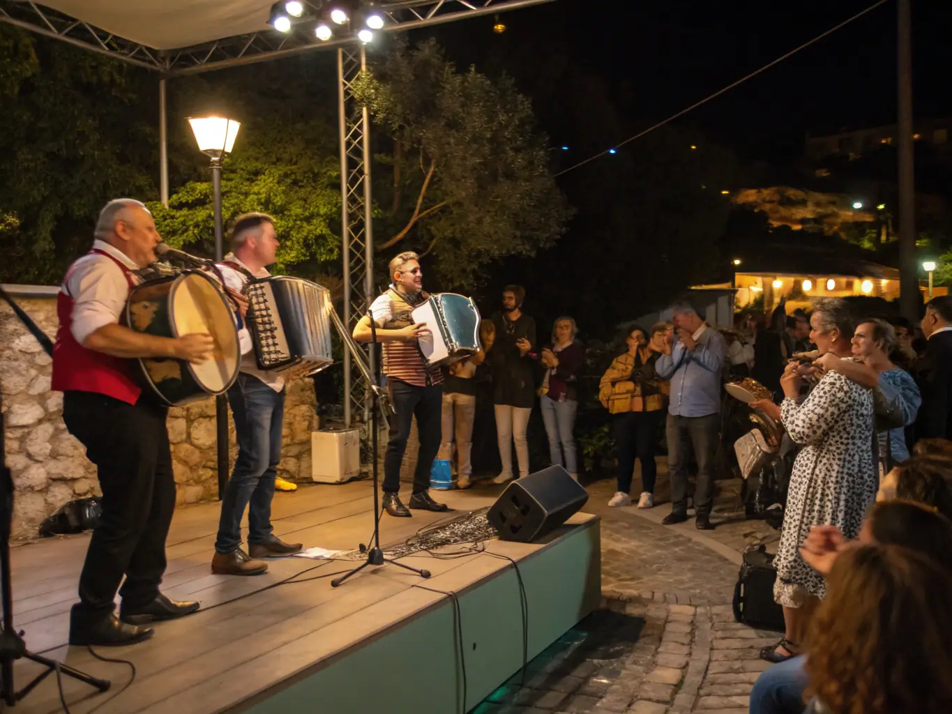 An image capturing a vibrant musical concert organized by ADAM ASSOC, featuring local musicians performing for an enthusiastic crowd in an outdoor setting.